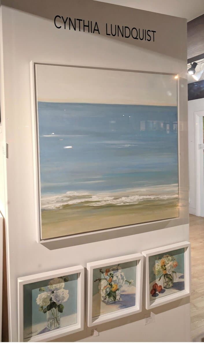 A wall of Cynthia Lundquist's framed paintings on exhibit, her name lettered above.