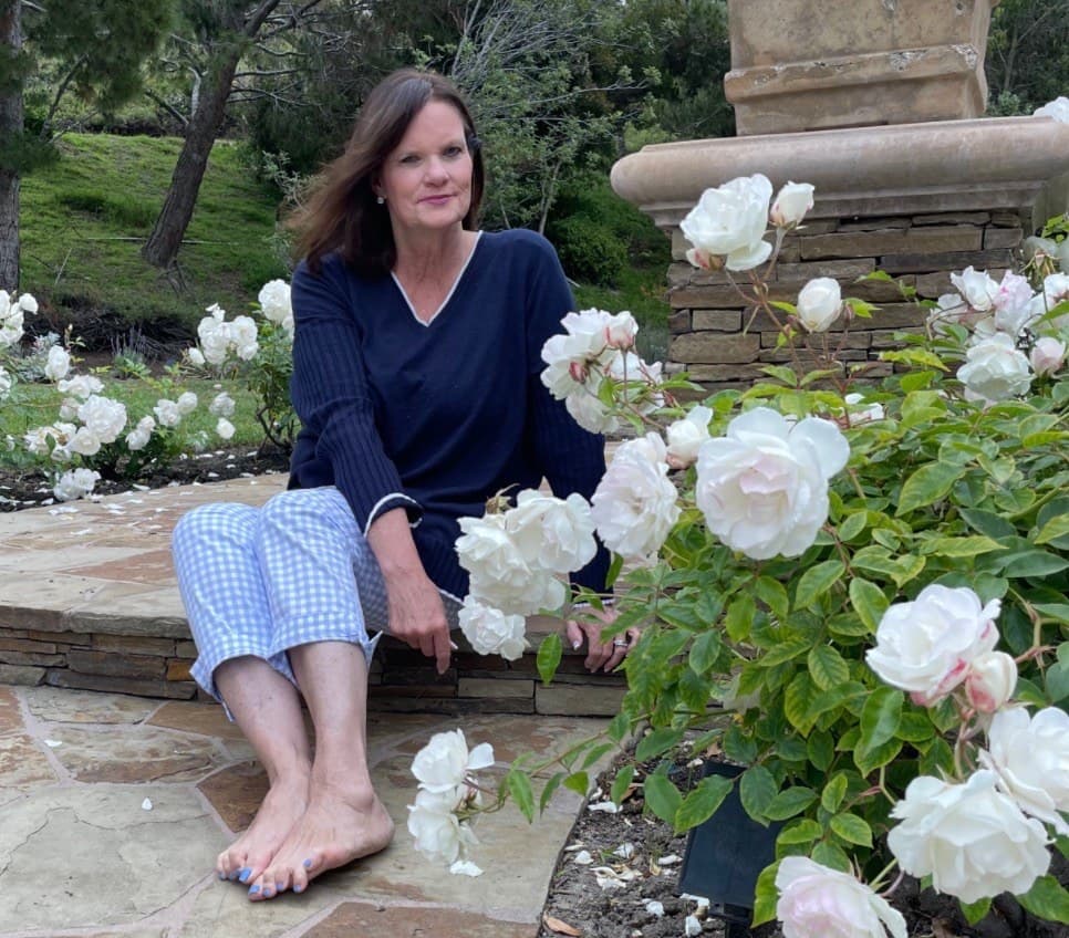 Cynthia Lundquist sitting on a stone garden step among white roses.